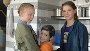 Jessi, Luis und Nina (Martha Fries, Emilio Sanmarino und Carolin Garnier) stehen lächelnd in einer Küche. © NDR/Studio Hamburg Foto: Romano Ruhnau