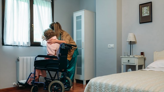 Eine Pflegerin schaut mit einer alten Frau, die im Rollstuhl sitzt, aus dem Fenster. © Colourbox Foto: 81162