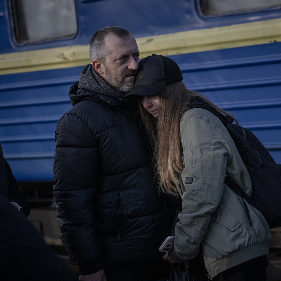 Zwei Flüchtlinge aus der Region Donezk im Osten der Ukraine stehen aneinandergelehnt vor einem Zug in den ukrainischen Nationalfarben. © picture alliance / Anadolu | Ozge Elif Kizil 
