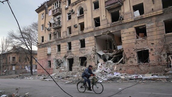 Ein Mann fährt mit dem Fahrrad an einem durch einen Angriff beschädigten Wohnhaus in Mariupol vorbei. © picture alliance/dpa/AP | Evgeniy Maloletka Foto: Evgeniy Maloletka