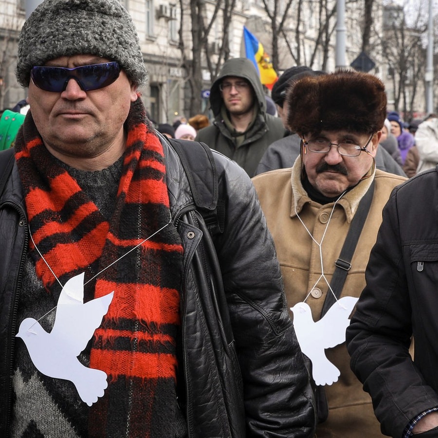 Männer, die weiße Tauben aus Papier um den Hals tragen, nehmen an einem Protest teil. © picture alliance/dpa/AP Foto: Aurel Obreja