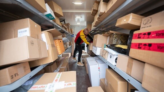 Ein DHL-Mitarbeiter sortiert in seinem Transporter die Pakete und Päckchen für die nächsten Zustellungen © picture alliance/dpa | Sebastian Gollnow 