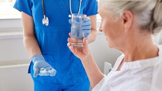 Eine Pflegekraft reicht einer im Bett liegenden Person Tabletten und ein Wasserglas © Picture Alliance | Zoonar | lev dolgachov Foto: Zoonar | lev dolgachov