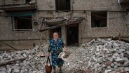 Eine Frau verlässt ihr Haus mit Habseligkeiten, nachdem eine Rakete den Wohnblock getroffen hat. © picture alliance/dpa/AP | Nariman El-Mofty 
