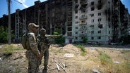 Russische Soldaten unterhalten sich in der Nähe eines Wohnhauses © picture alliance/dpa/AP | Uncredited 