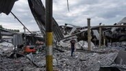 Ein Anwohner inspiziert die Trümmer seiner Getränkefabrik, die in der vergangenen Nacht von einer russischen Rakete zerstört wurde. © picture alliance/dpa/AP | Evgeniy Maloletka 