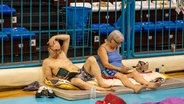 Zwei Urlauber sitzen in einer Notunterkunft auf dem Boden © picture alliance/dpa/InTime News/AP | Lefteris Damianidis 