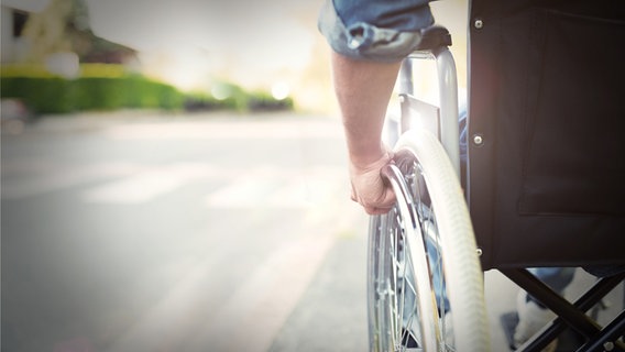 Ein Mann hält mit seiner Hand einen Rollstuhl-Rad © panthermedia Foto: minervastock