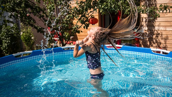 Ein Mädchen badet in einem Gartenpool, wirft ihren Kopf in den Nacken und schleudert Wasser aus ihren langen Haaren. © photocase.de Foto: Westend61