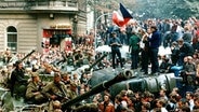 August 1968, Tschechoslowakei, Prag: Protestierer umringen in der Innenstadt sowjetische Panzer und stehen mit einer Fahne der Tschechoslowakei auf einem umgekippten Militärfahrzeug. © picture alliance/Libor Hajsky/CTK via epa/dpa 