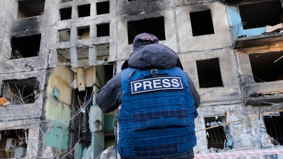 Ein Journalist steht vor einem zerbombten Gebäude in der Ukraine. © picture alliance/abaca Foto: Alfred Yaghobzadeh