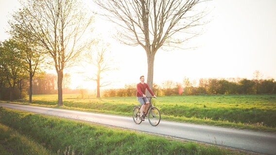 Ein Mann radelt im Morgenlicht auf einer Landstraße entlang. © Photocase Foto: David-W