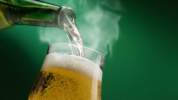 Bier fließt aus einer Flasche in ein Glas und dampft. © NDR 