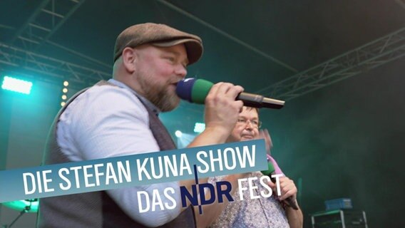 Stefan Kuna von NDR 1 Radio MV steht mit Schiebermütze und Mikrofon auf der Bühne © NDR Foto: NDR