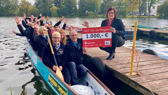 Mitglieder des Drachenbootvereins Parchim sitzen in einem Drachenboot und freuen sich über einen Scheck über 1.000 Euro. © NDR Foto: Jan Baumgart
