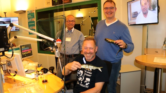 Karl-Heinz Brillowski, Heinz Galling und Ralf Markert stehen mit Angelausrüstung im Studio von NDR 1 Radio MV.  