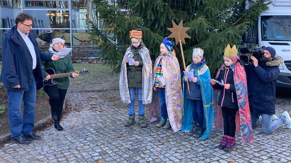 Vier als Sternensinger verkleidete Kinder stehen in Begleitung Erwachsener und des Landesfunkhausdirektors vor dem Landesfunkhaus Schwerin. © ndr.de Foto: Andreas Lußky