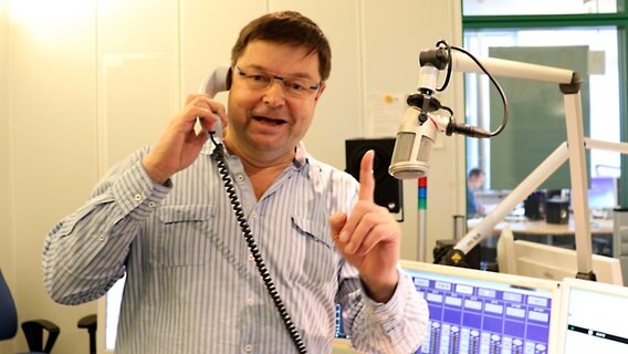 Leif Tennemann hält im Studio von NDR 1 Radio MV einen Telefonhörer in der Hand.  