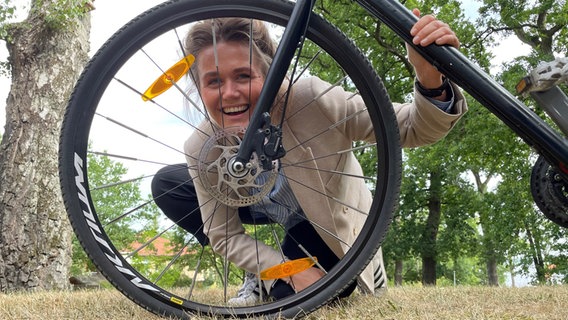 eine junge Frau hockt hinter einem Fahrrad und blickt durch Rahmen und Speichen © NDR Foto: Christian Kohlhof