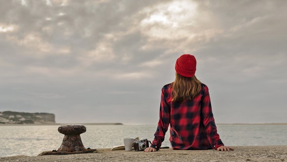 Eine Frau sitzt auf einer Kaimauer und schaut auf Meer und Küste © colourbox 