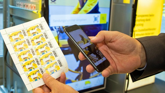 Ein Mann scannt mit seinem Smartphone den Matrix-Code einer digitalen Briefmarke. © Deutsche Post AG 