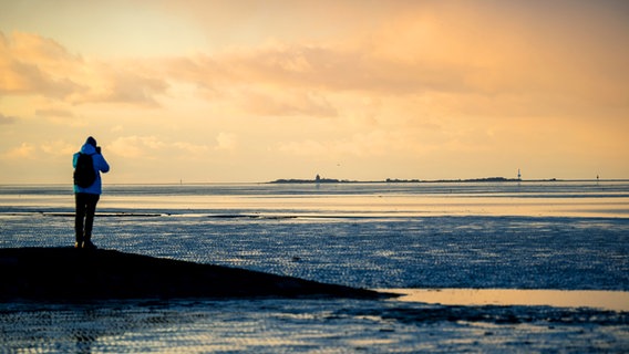 Ein Spaziergänger steht im Watt vor Cuxhaven und fotografiert die Insel Neuwerk. © picture alliance/dpa Foto: Sina Schuldt