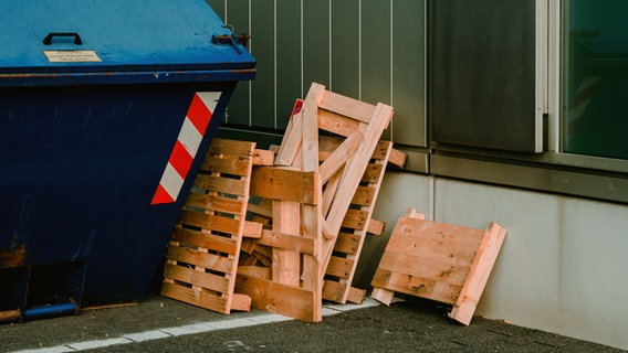 Palettenreste liegen neben einem Müllcontainer. © Photocase Foto: Z2sam