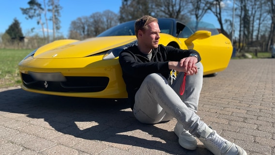 Mann sitzt nachdenklich angelehnt an einen gelben Ferrari. © NDR 