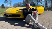Mann sitzt nachdenklich angelehnt an einen gelben Ferrari. © NDR 