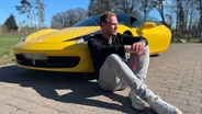 Mann sitzt nachdenklich angelehnt an einen gelben Ferrari. © NDR 