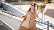 Eine Frau steht mit einem Kaffeebecher an einem Geländer in der Sonne. © Colourbox Foto: Mykola