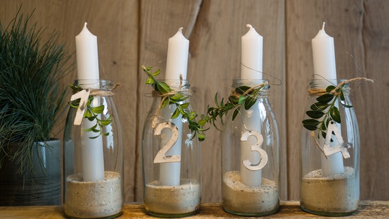 Weiße Kerzen stecken in Wasserflaschen, die mit Sand gefüllt sind. © NDR Foto: Anja Deuble