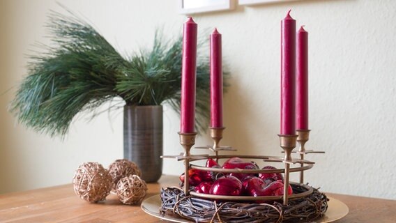 Vier rote Kerzen in einem goldenen Kerzenring auf einem golden Teller. © NDR Foto: Anja Deuble