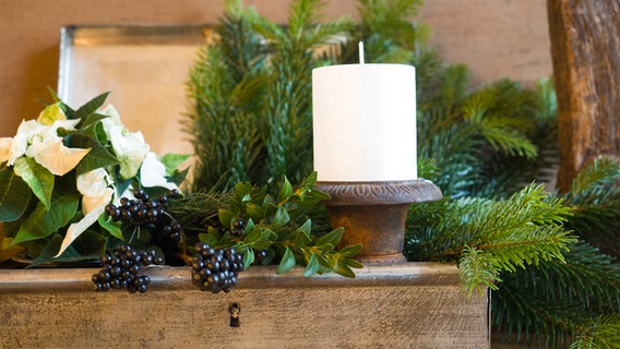Eine Kiste gefüllt mit Tannenzweigen, Weihnachtsstern und Kerze. © NDR Foto: Anja Deuble