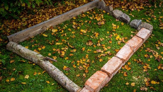 Steine, Holzlatten und Äste liegen auf dem Boden und bilden den Rahmen für ein Beet. © NDR Foto: Udo Tanske