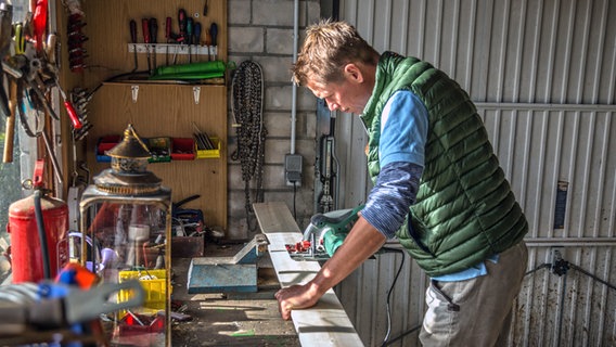 Gärtner Peter Rasch steht in seiner Werkstatt und baut Futterstationen für Vögel. © NDR Foto: Udo Tanske