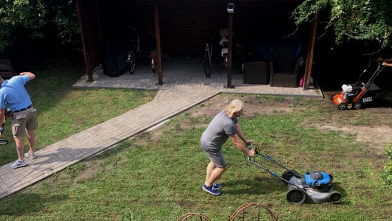 Die Fläche in einem Hinterhof wird für die Verlegung eines Rollrasens vorbereitet: Ein Mann mäht den vorhandenen Rasen ganz kurz. © NDR 