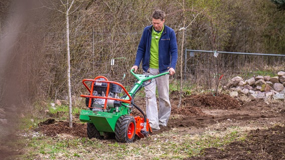 Um den Boden für den neuen Rasen vorzubereiten geht Peter Rasch mehrfach mit einer Gartenfräse über den Boden. © NDR Foto: Udo Tanske