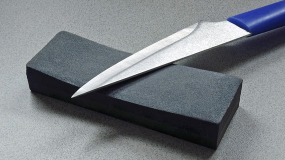 Auf einem kleinen dunklen Schleifstein liegt ein Messer. © imago/Steinach 