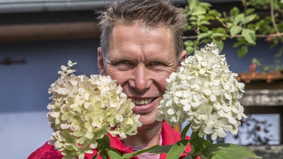 Peter Rasch hält weiß blühende Hortensien-Dolden vor sein Gesicht. © NDR Foto: Udo Tanske
