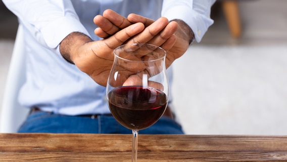Ein Mann kreuzt die Hände vor einem Glas Wein. © Imago/Panthermedia Foto: Andrey Popov