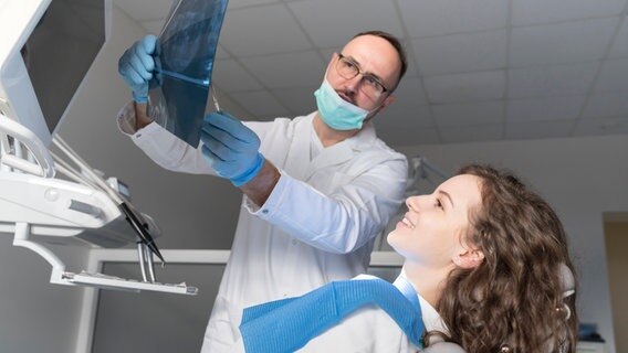 Ein Zahnarzt erklärt einer Patientin die Röntgenaufnahmen. © imago images / Westend61 