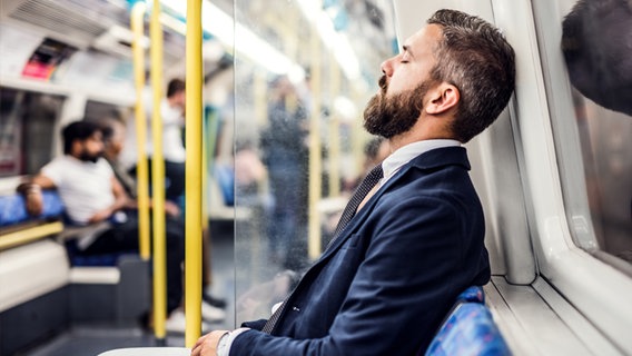 Ein jüngerer Mann mit Bart und Anzug sitzt mit geschlossenen Augen in einer U-Bahn. © Colourbox Foto: -