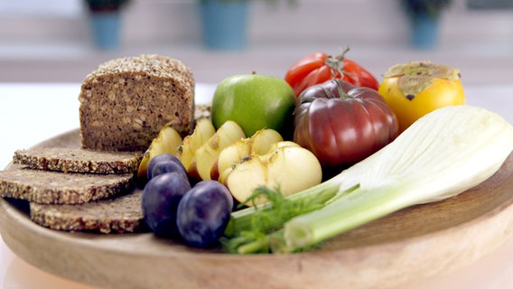 Vollkornbrot, Obst und Gemüse liegen auf einem Holzbrett. © NDR 