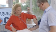 Bewegungs-Doc Melanie Hümmelgen misst den Blutdruck eines Patienten. © NDR 