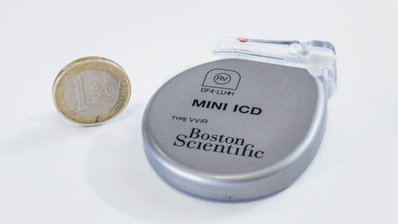 Ein implantierbarer Kardioverter-Defibrillator neben einem Ein-Euro-Stück. © picture alliance_imageBROKER_Jochen Tack 