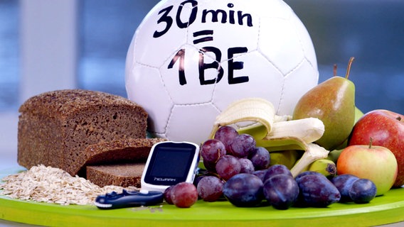 Obst, Brot, Getreide und ein Insulinmessgerät liegen auf einem Tisch, im Hintergrund liegt ein Fußball. © NDR 