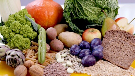 Verschiedene Obst- und Gemüsesorten sowie Vollkornbrot und Nüsse auf einem Tisch. © NDR 
