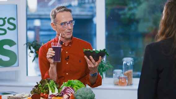 Ernährungs-Doc Matthias Riedl spricht mit seiner Patientin. Er hält einen Smoothie und eine Schale mit Salat in den Händen. © NDR Foto: Oliver Zydek/Moritz Schwarz