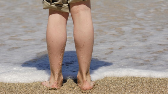 Blick auf die Waden von hinten eines Kindes, das am Strand steht. © picture alliance Foto: Peter Carroll